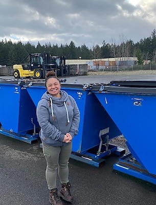 A woman poses in front of three garbage cans.