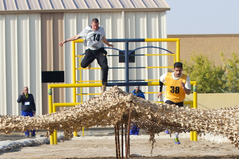 One athlete jumps over an obstacle as another sprints.