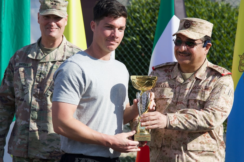 A soldier smiles for a photo as he receives a trophy from a foreign officer.