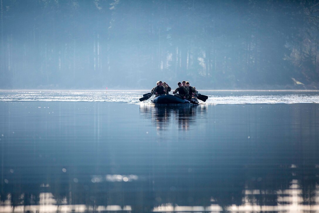 Army cadets travel through water in a small inflatable boat.