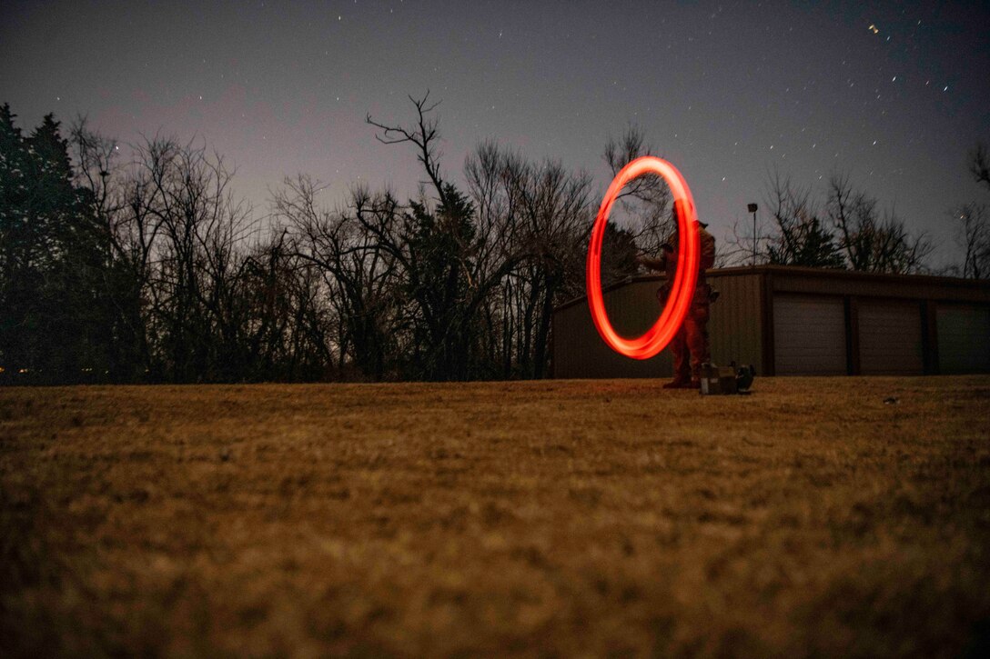 A guardsman draws a circle using a red light at night.