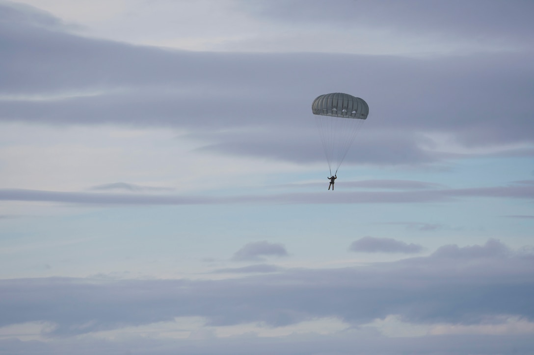 An airman descends in the sky wearing a parachute.