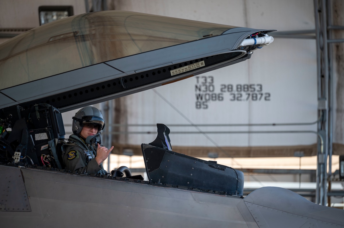 A pilot signals a hand gesture in the cockpit of an F-22 Raptor