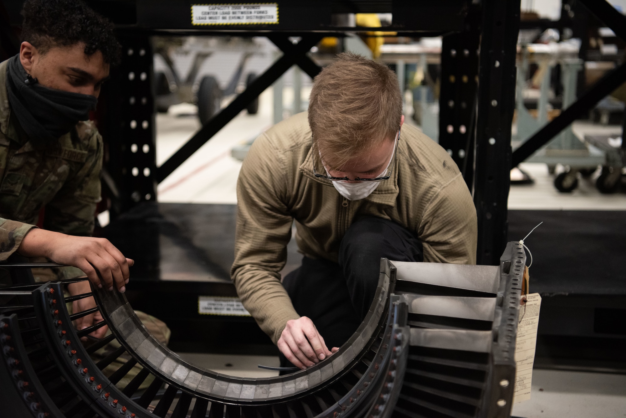 Two Airmen work on an engine piece.