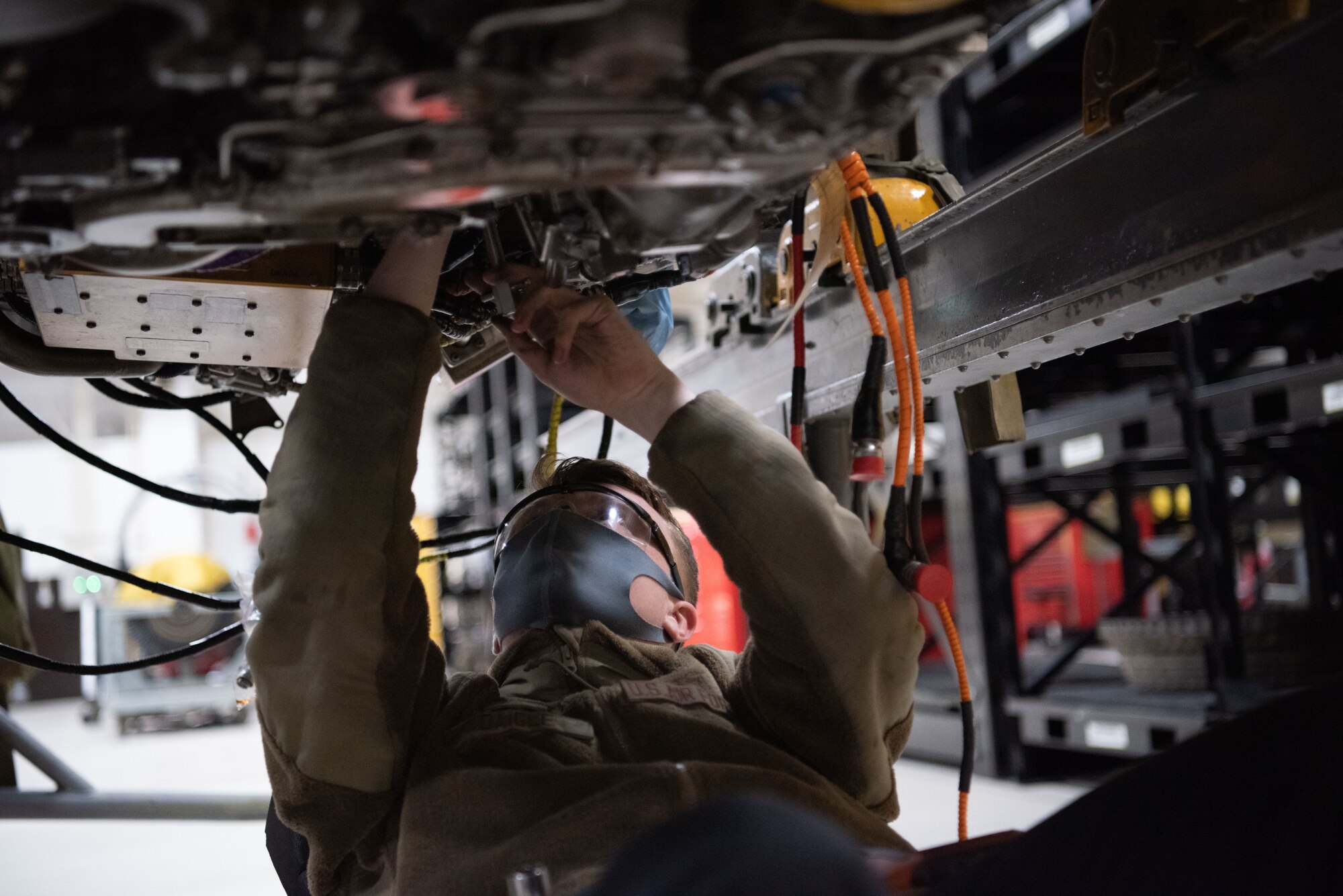 An Airman rolls under a jet engine to fix it.