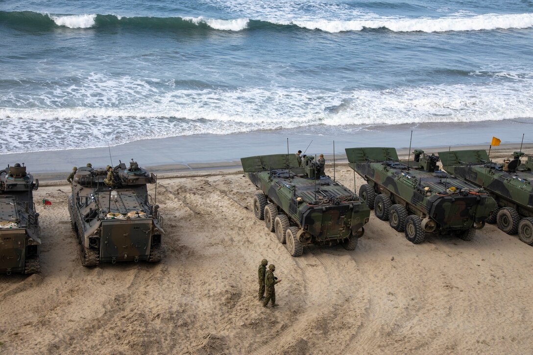 A group of military vehicles sit on a beach.
