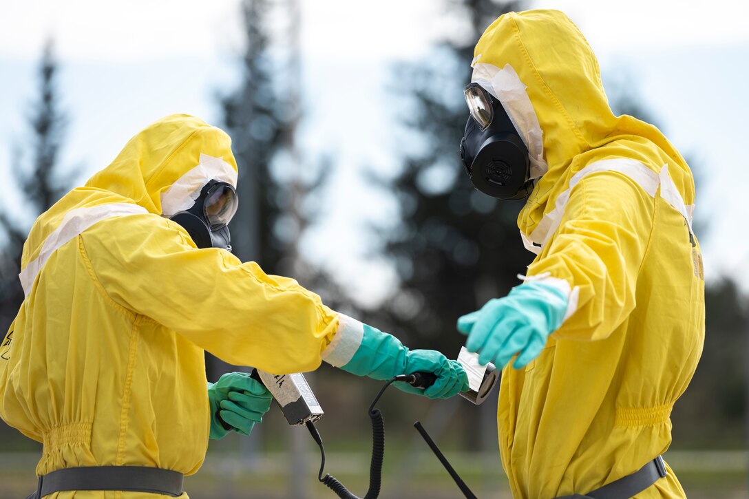 One airman dressed in protective clothing scans another airman in protective gear.