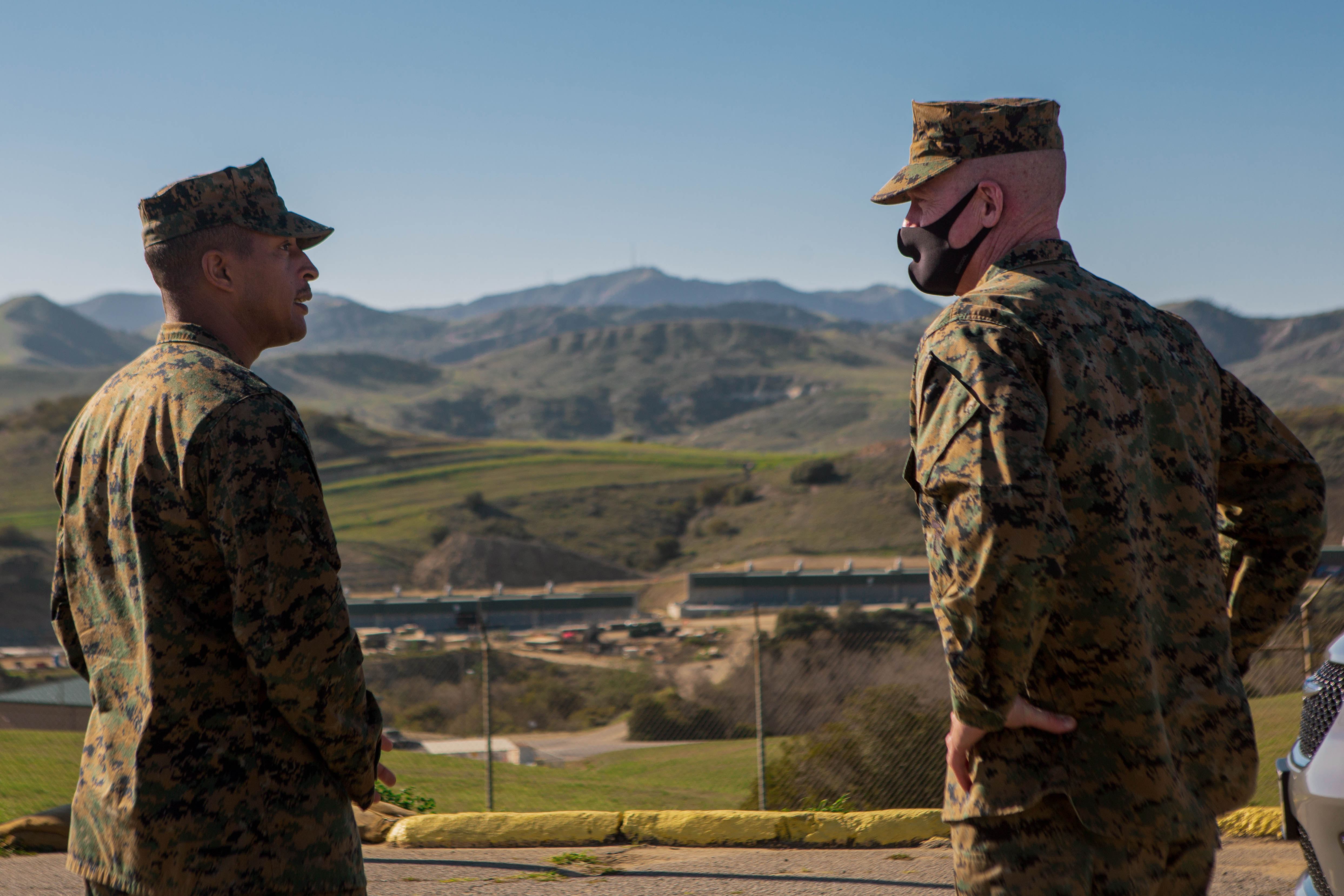 Two Marines talking in front of a scene of mountains, with their backs to the camera.