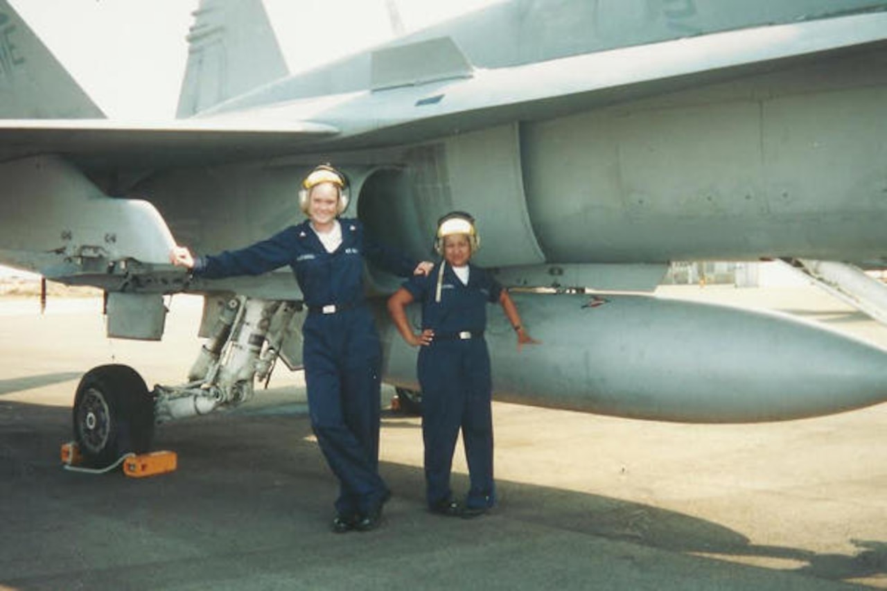 Two women stand next to an aircraft.