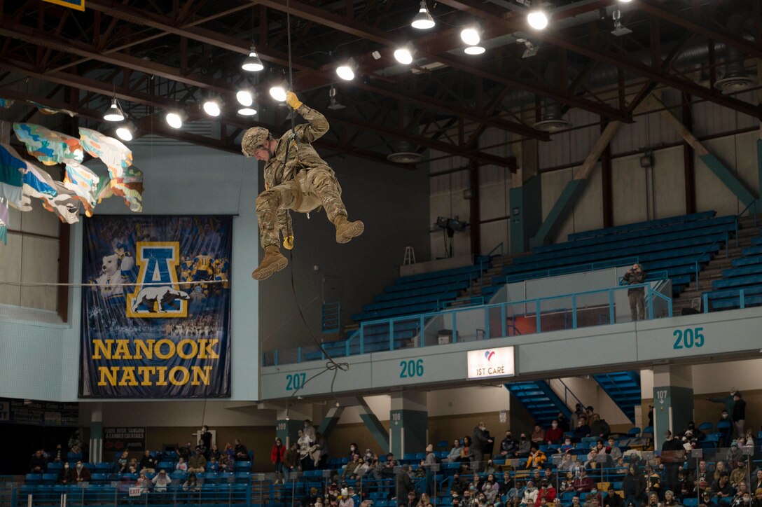 A soldier rappels from a ceiling during a hockey game.