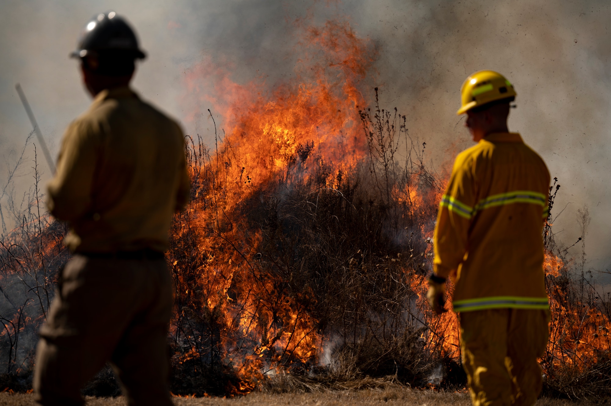 Two firefighters observe a controlled fire.