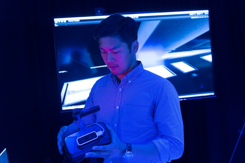 A young man holds a device while standing in a dark room.