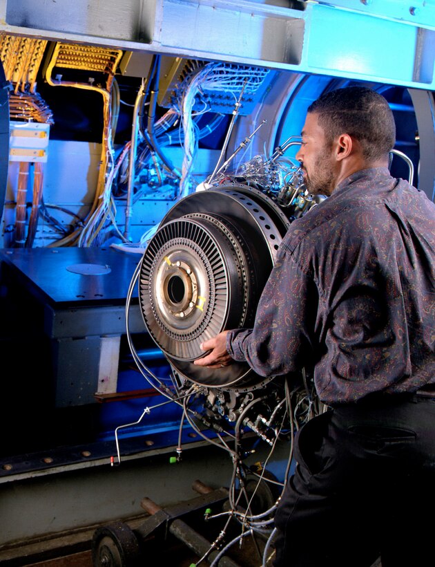A man touches a cylinder in a room with electronic equipment.