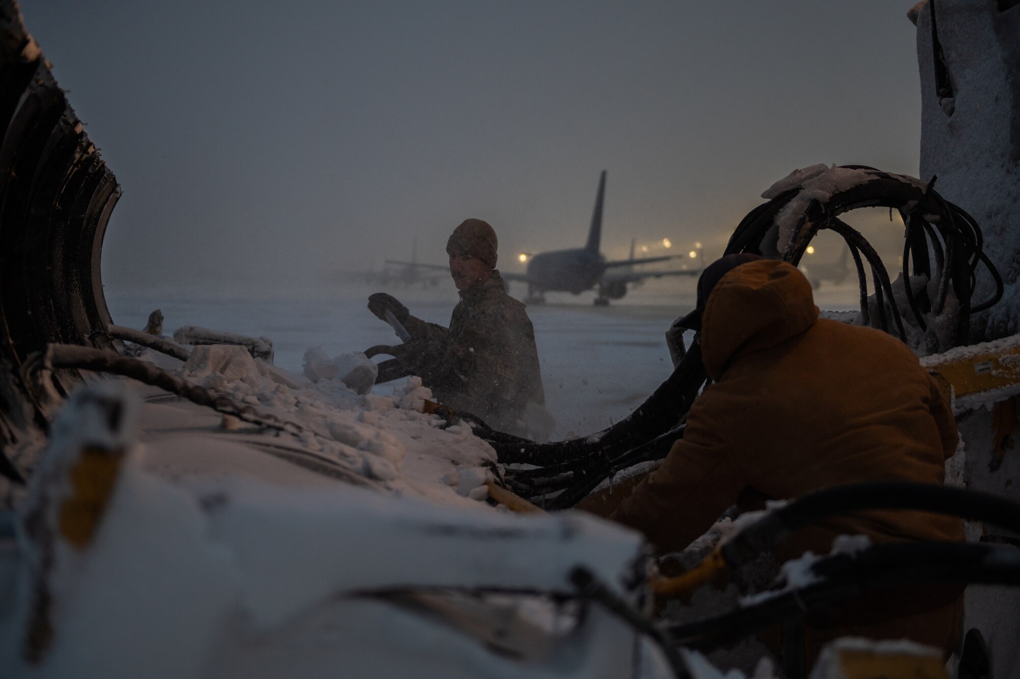 Senior Airman Trent Schroedl, structural journeyman, and Mr. Bryce Schroeder, structural systems maintenance mechanic, both assigned to the 22nd Civil Engineering Squadron’s snow removal team, clear snow from an Oshkosh Snow Plow Feb. 17, 2022, at McConnell Air Force Base, Kansas.