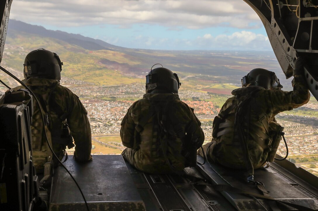 Three soldiers ride on the back of a helicopter.