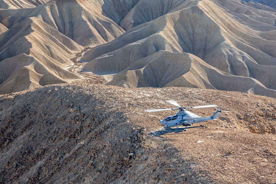 A helicopter sits in a hilly area in desert-type terrain.