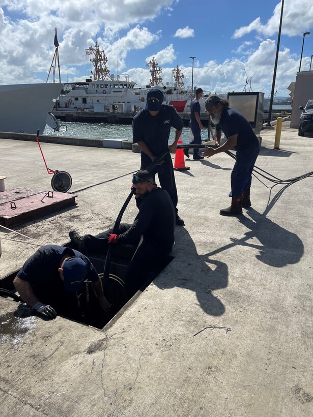 Members of Base San Juan pull cable through electrical conduit.