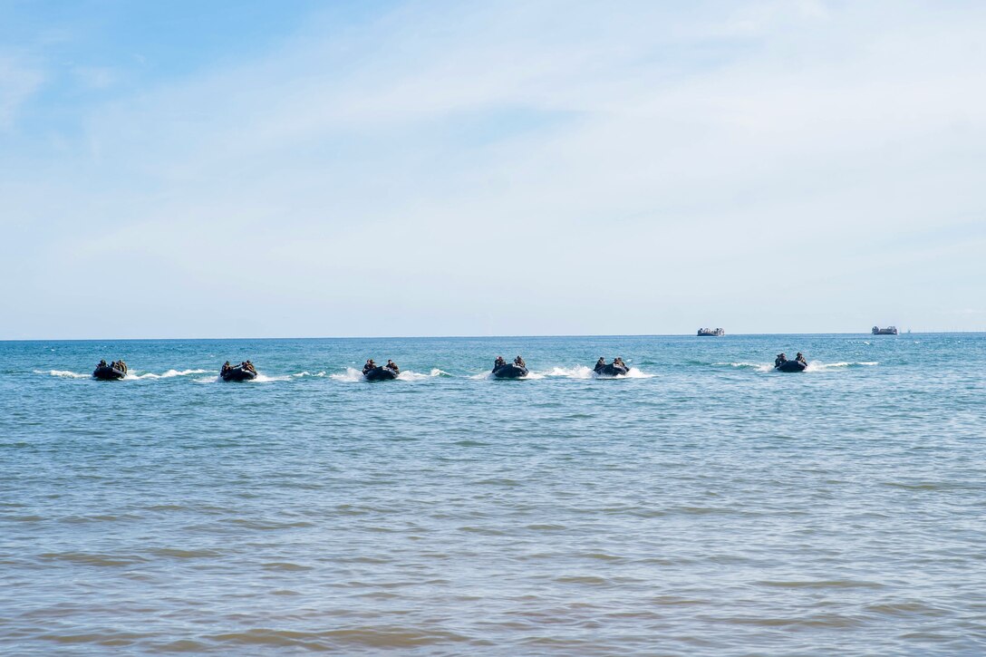 A line of inflatable boats head to shore.