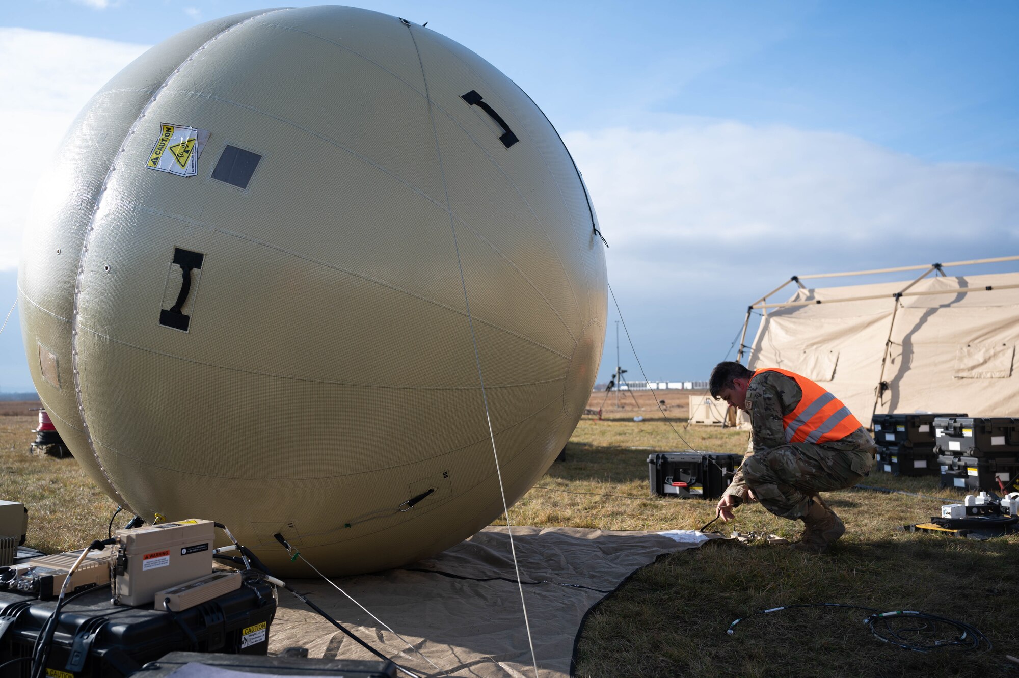 An Airman kneels next to a ground antenna transmit and receive ball.
