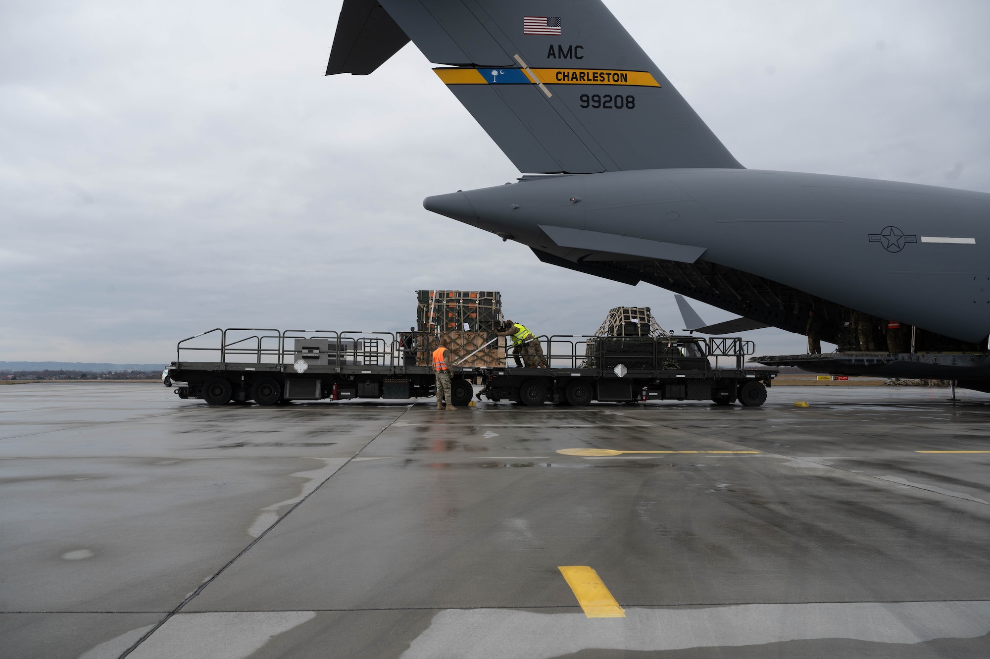 Airmen push a pallet of cargo from one cargo loader onto another.