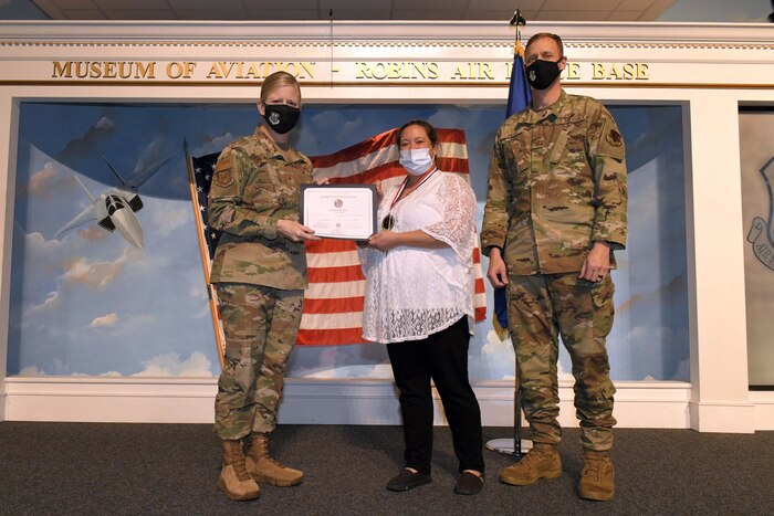 Photo shows individual standing with certificate between two other people.