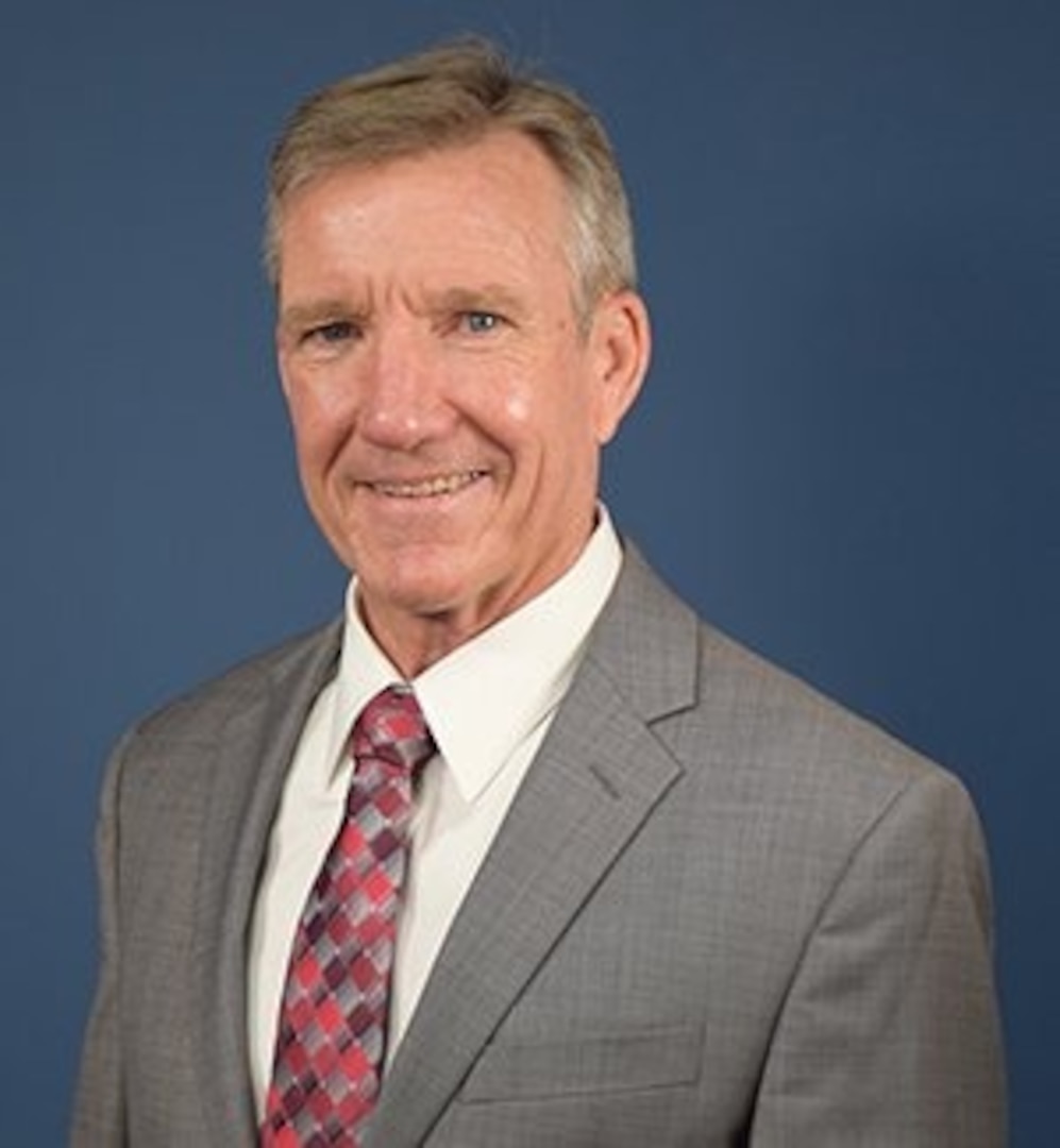 Man in brown tweed style suit with blue background.