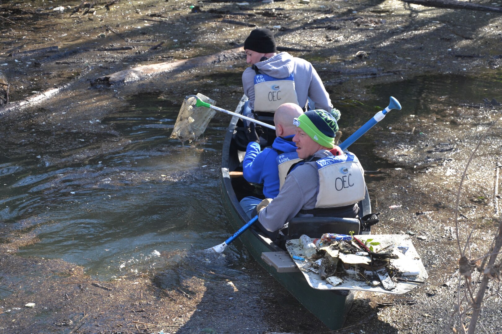 Three men in canoe pick up trash from creek.