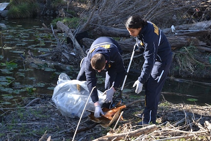 Two people pick up trash from a creek.