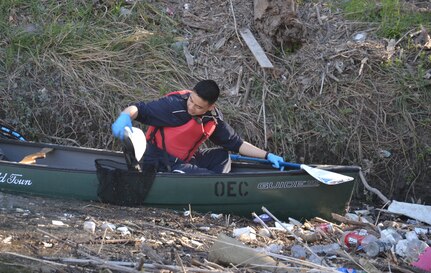 Man picks trash out of water from canoe.