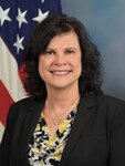 Black haired woman, smiling with black suit jacket and speckled top with a US Flag behind her.