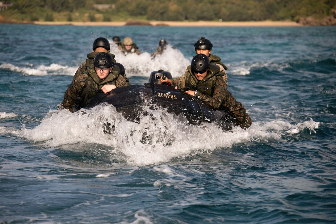 Marines ride in two small boats in a body of water.