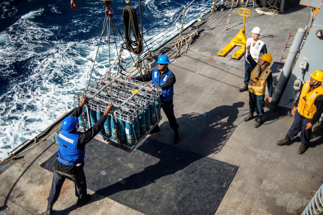 Sailors receive cargo aboard a ship at sea.