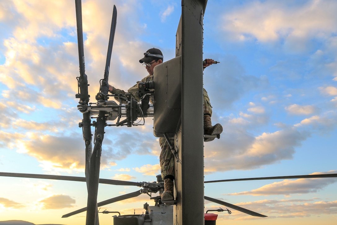 A soldier stands atop a helicopter while performing work on it.