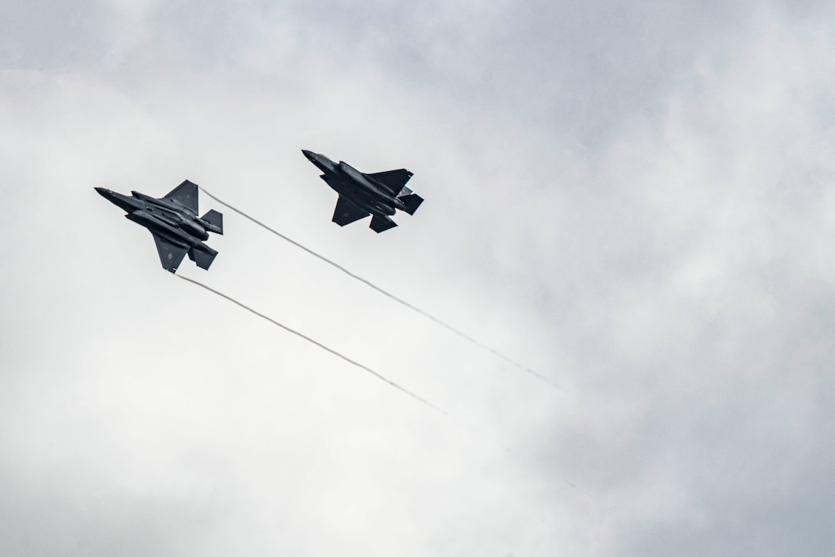 Two Air Force jets fly in a grey cloudy sky.