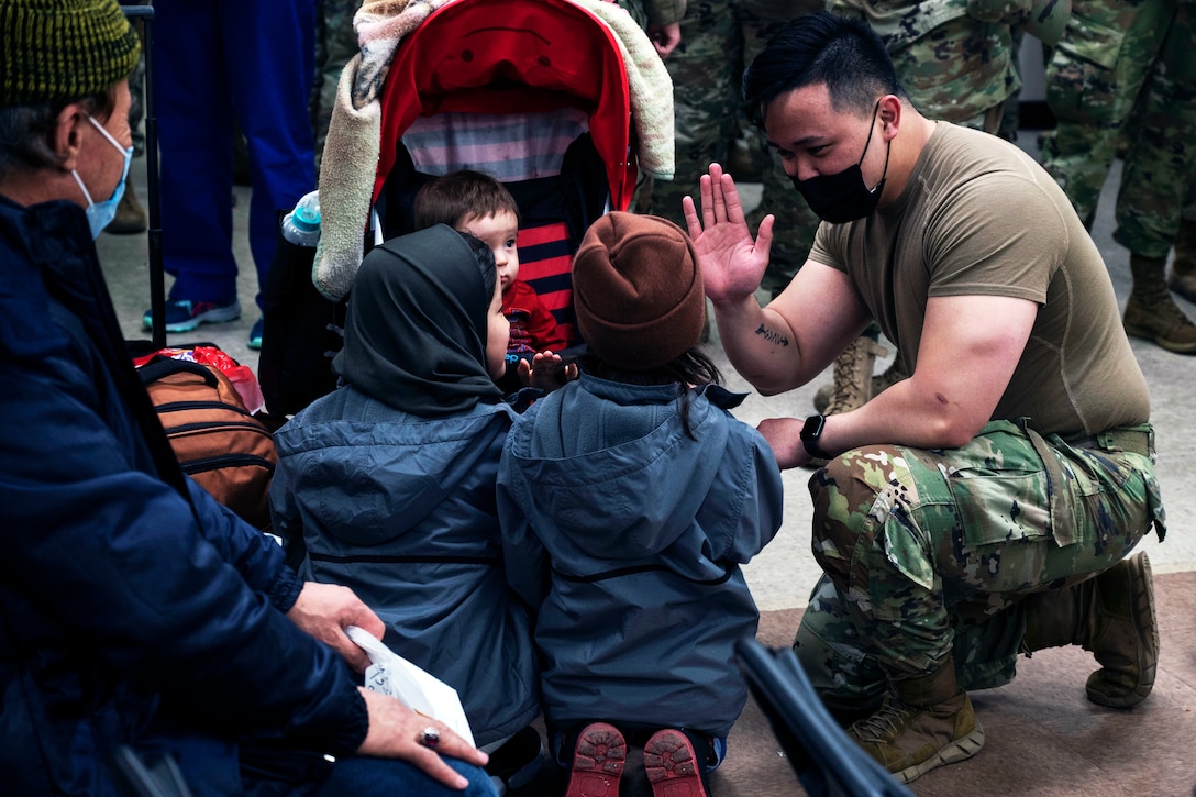 A soldier wearing a face mask kneels to say goodbye to an Afghan family.