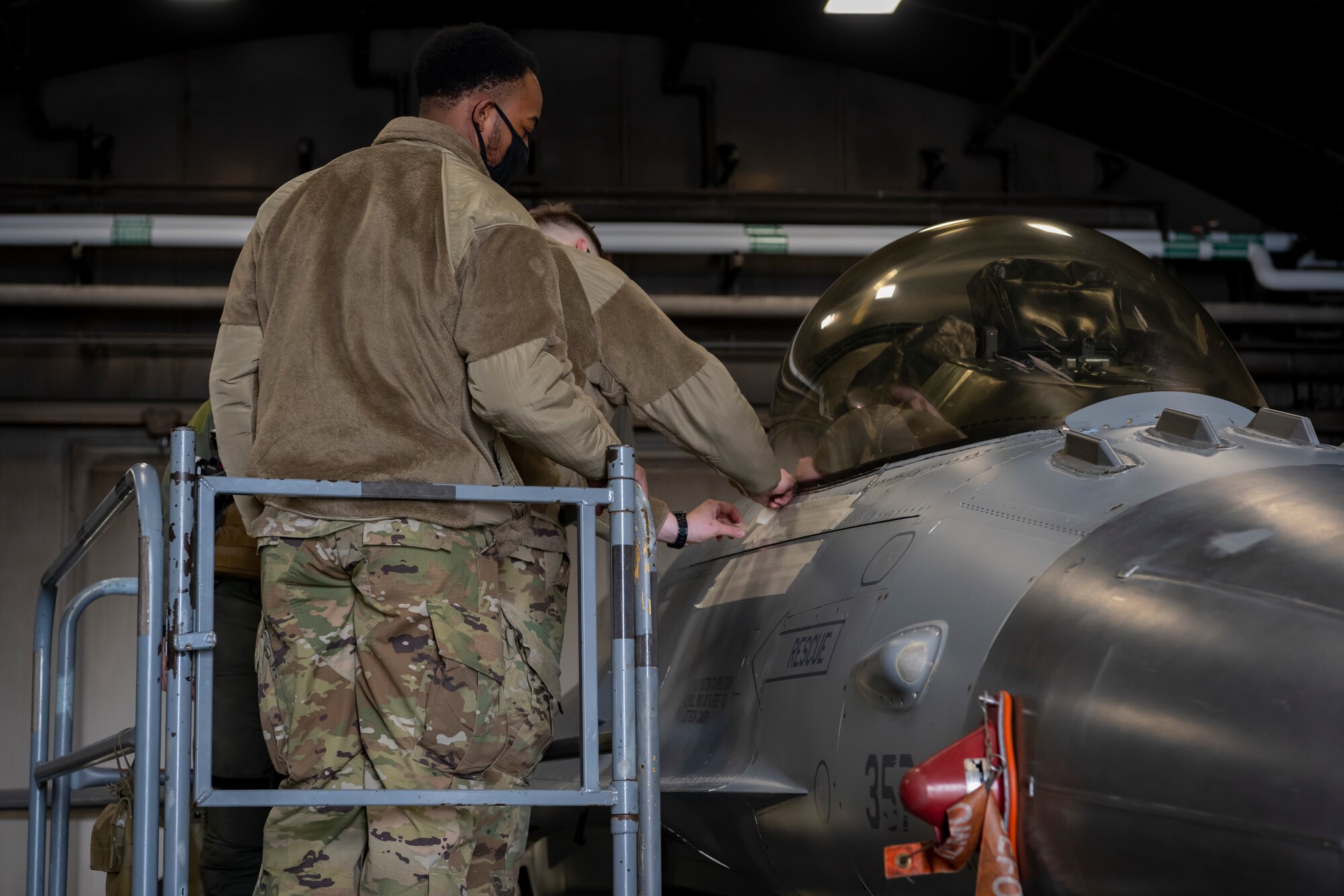 Airmen removing tape from the side of an F-16 Fighting Falcon.