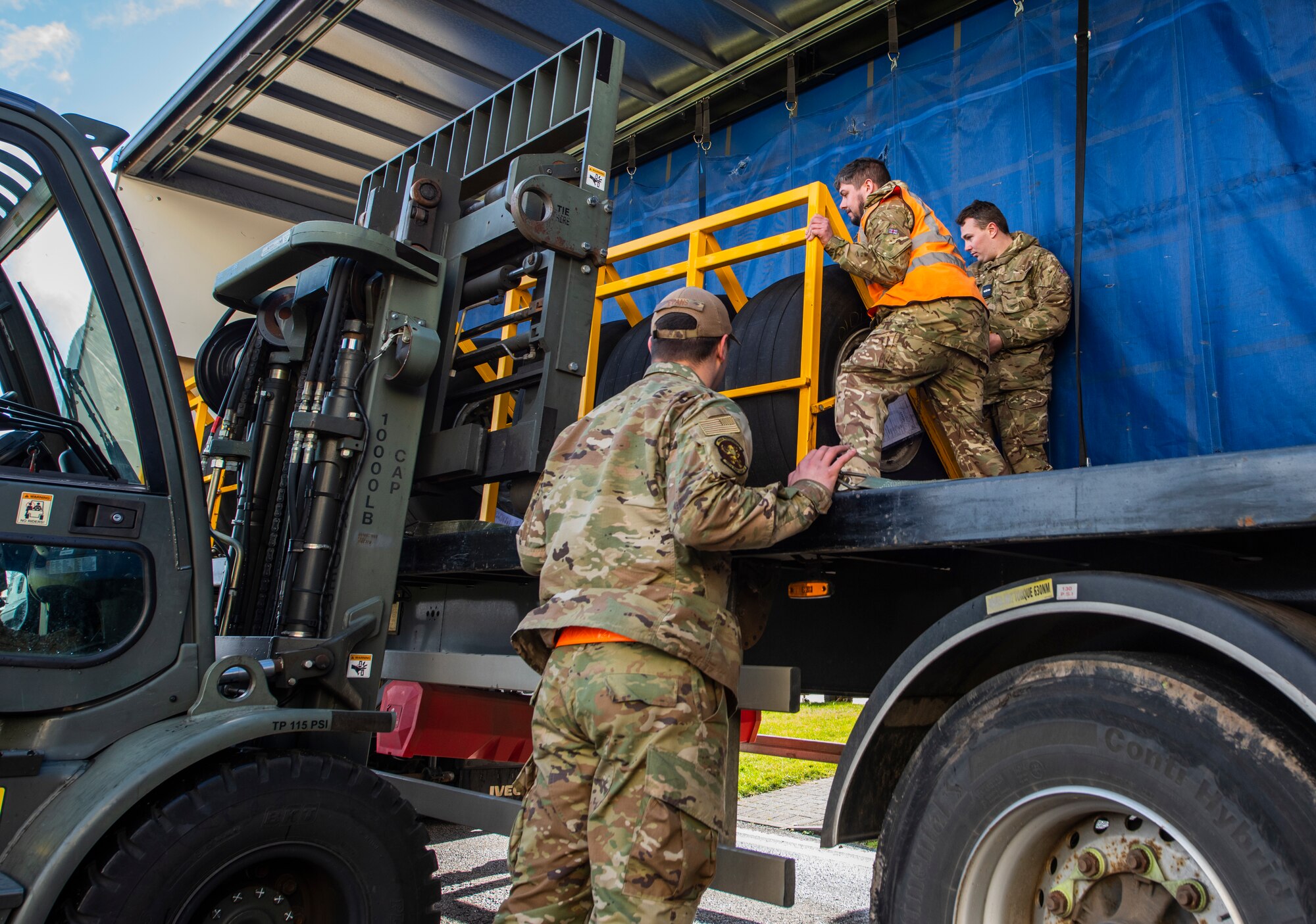 A 100th Aircraft Maintenance Squadron Airman and members of the Royal Air Force from RAF Brize Norton work together to guide a rack of C-17 Globemaster III aircraft wheels onto a forklift at RAF Mildenhall, England, Feb. 24, 2022. Airmen from the 100th AMXS are supporting our host nation partner by preparing 12 C-17 wheels for disassembly so that they can be reused in the future. (U.S. Air Force photo by Senior Airman Kevin Long)