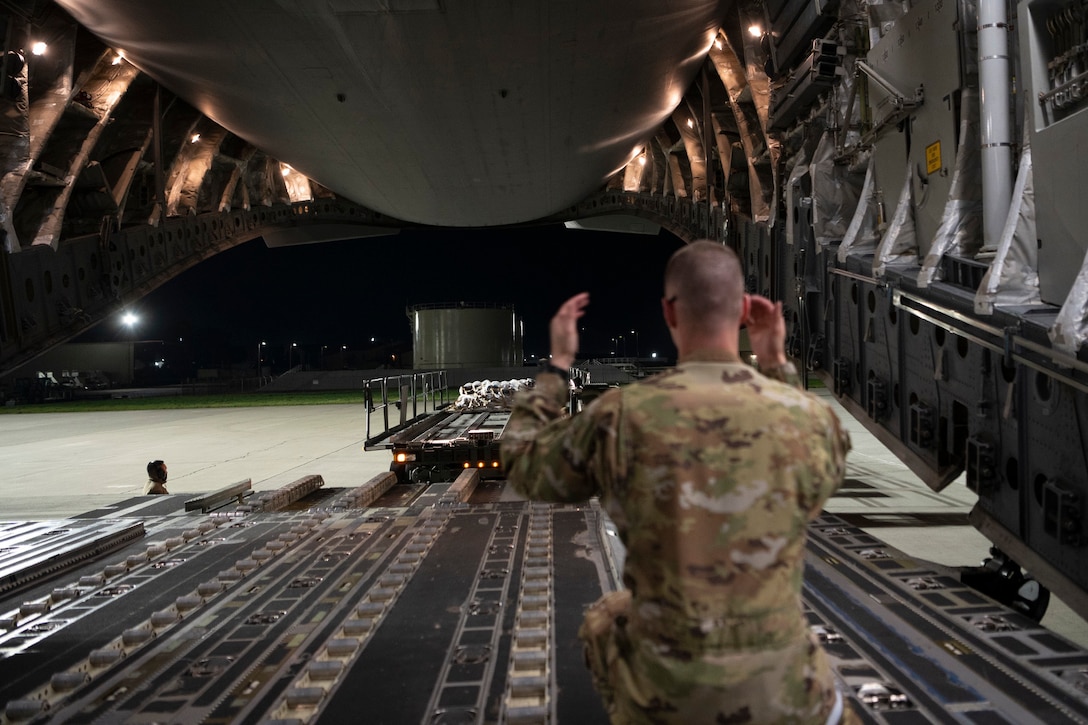 An airman guides a large loading vehicle toward the opening of an aircraft.