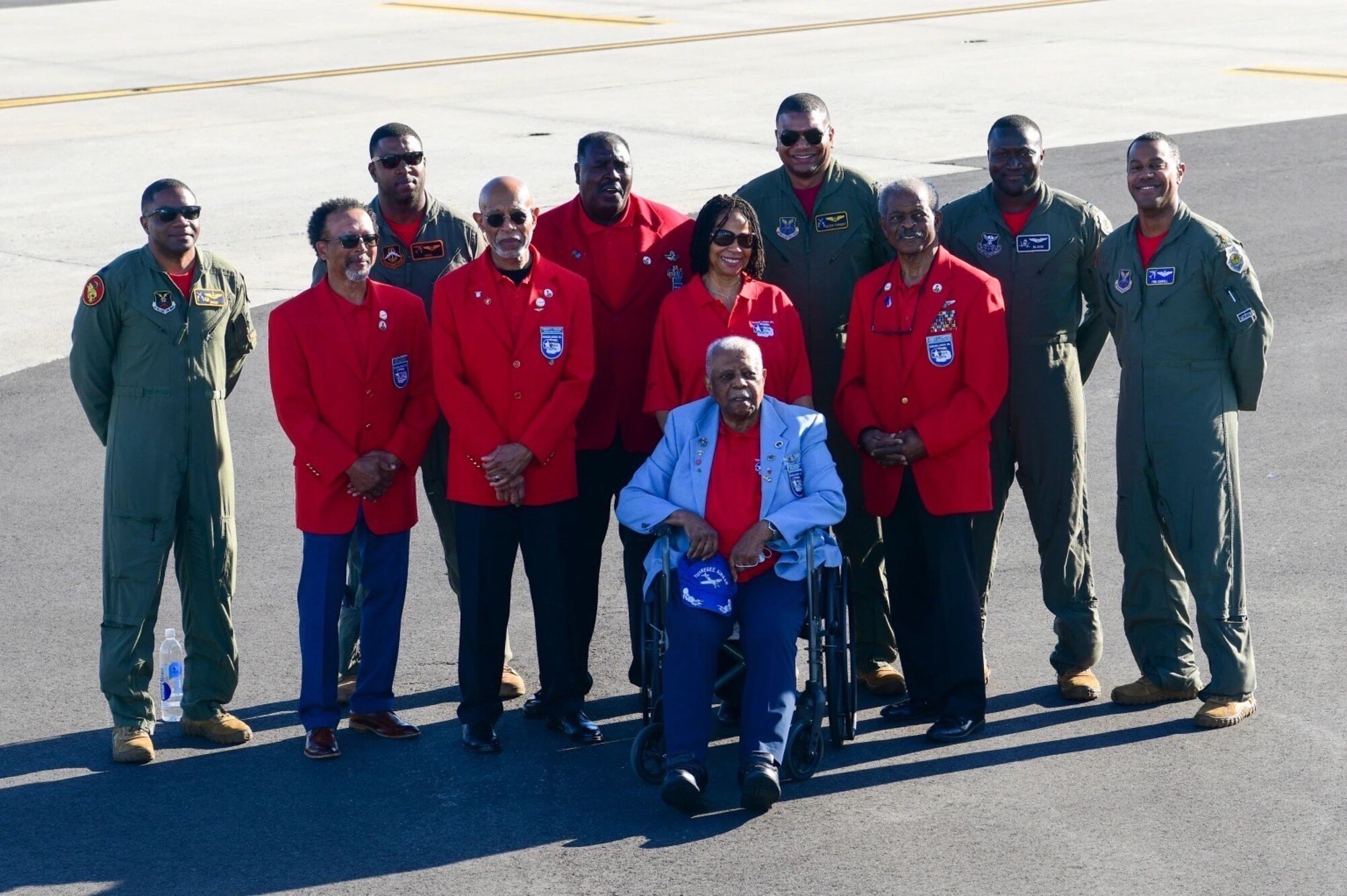 Eleven people stand smiling next to each other on a flight line.