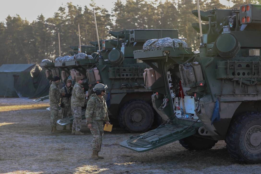 Four soldiers walk around two tactical vehicles.