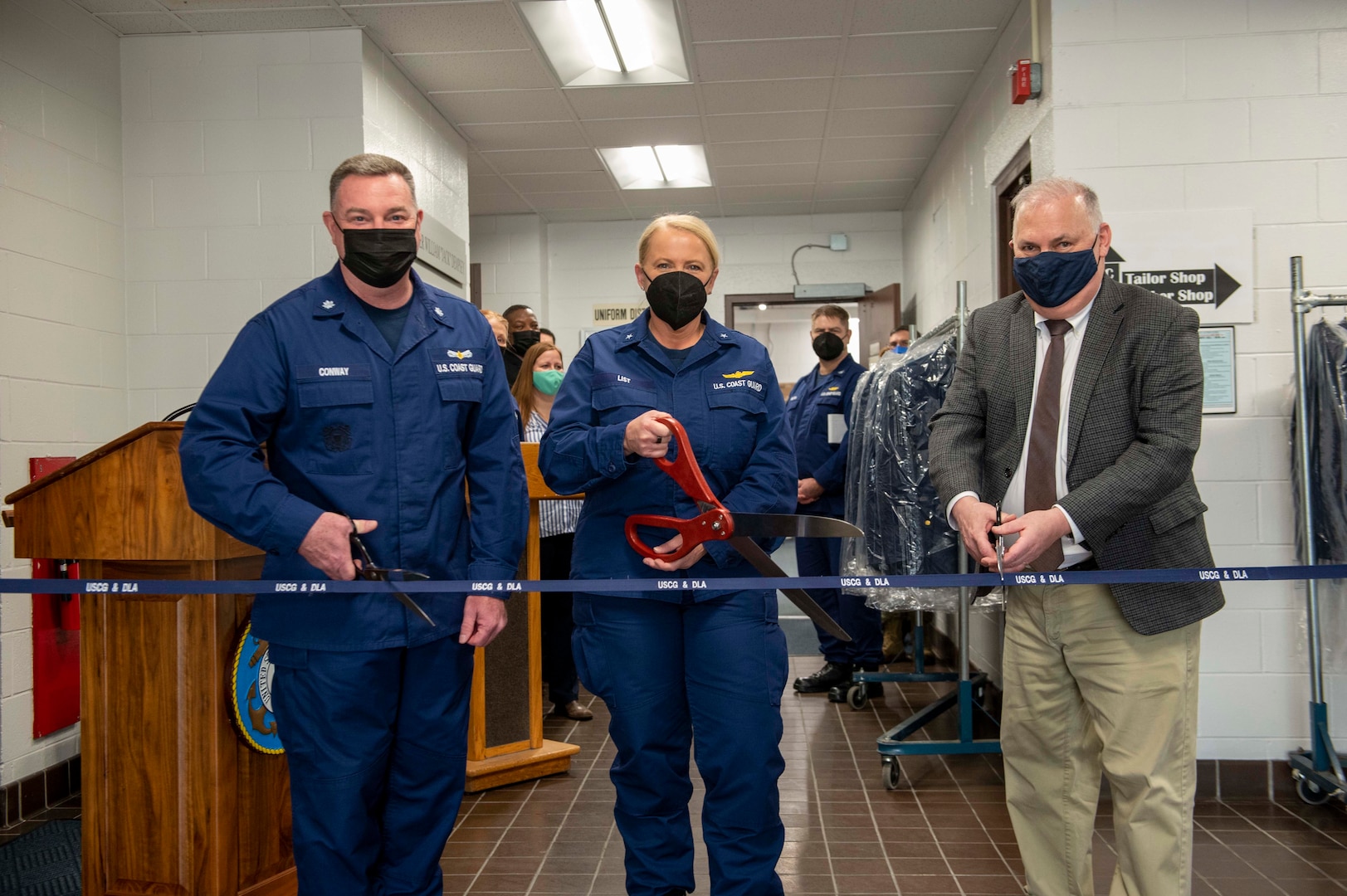 uniformed man and woman and civilian man cut ribbon