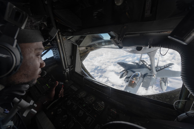 An airman operates a refueling boom to a jet.