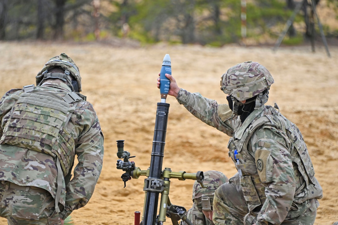 A soldier loads a weapon as another soldier kneels beside.