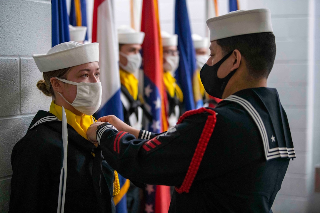 A sailor adjusts the uniform of a recruit.