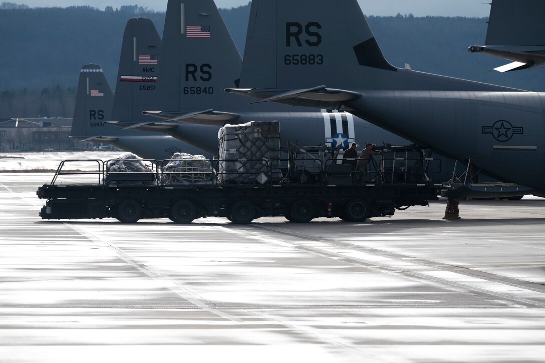 A loader moves baggage and supplies onto a C-130J Super Hercules aircraft on a flightline.