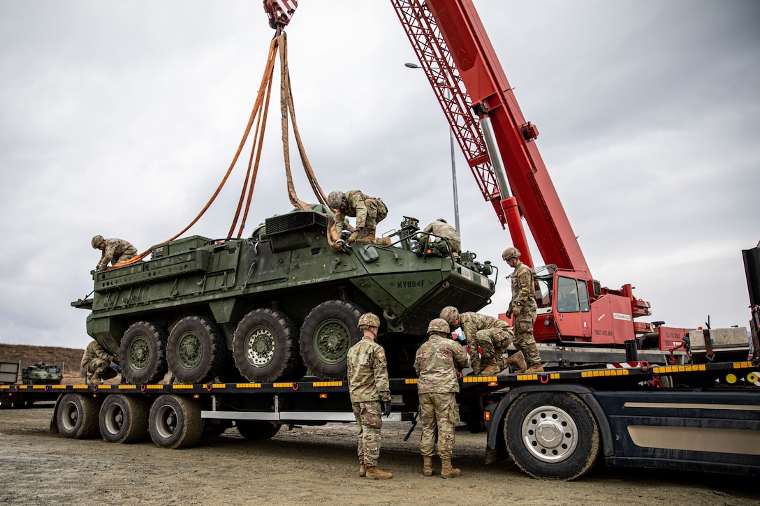 Army soldiers secure hooks to an armored vehicle.