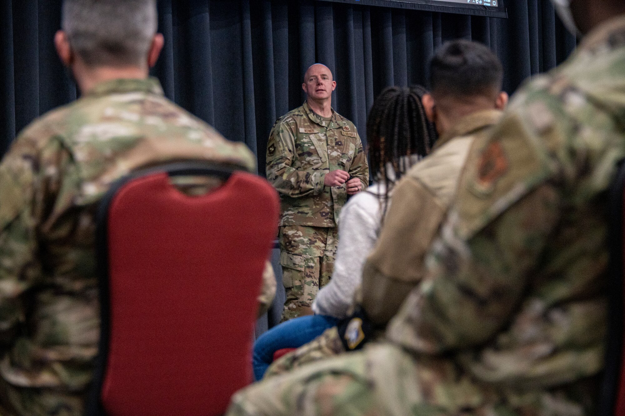 Man stands in front of crowd sitting in chairs.