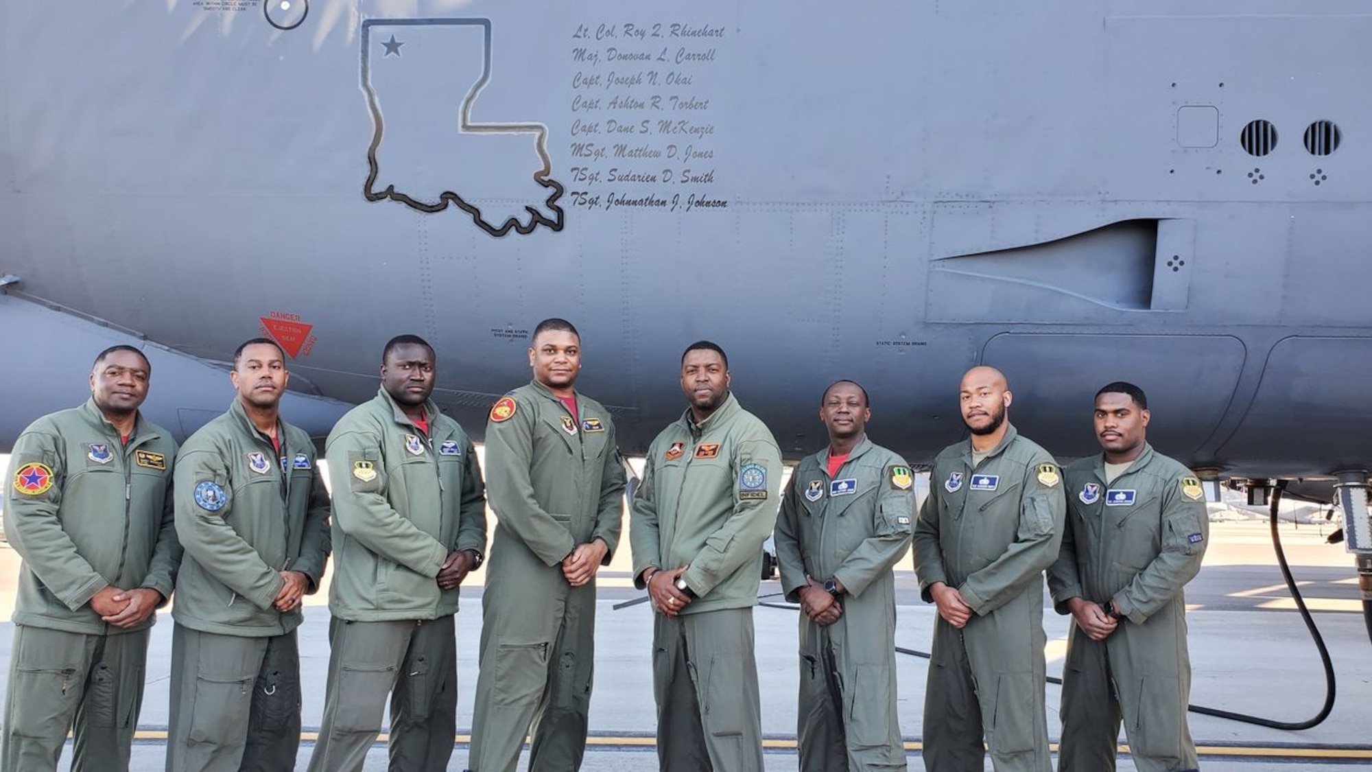 Eight men stand near an aircraft.