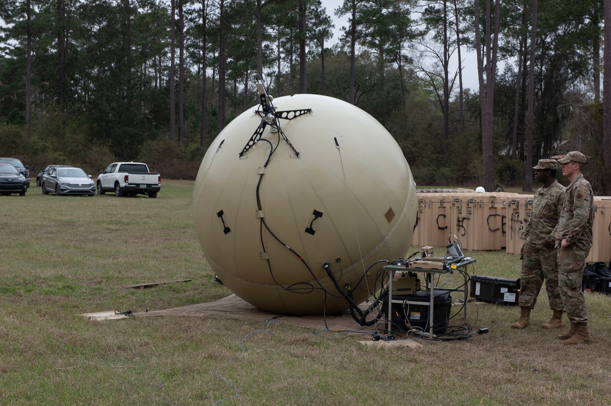 Two Airmen stand in front of a satellite