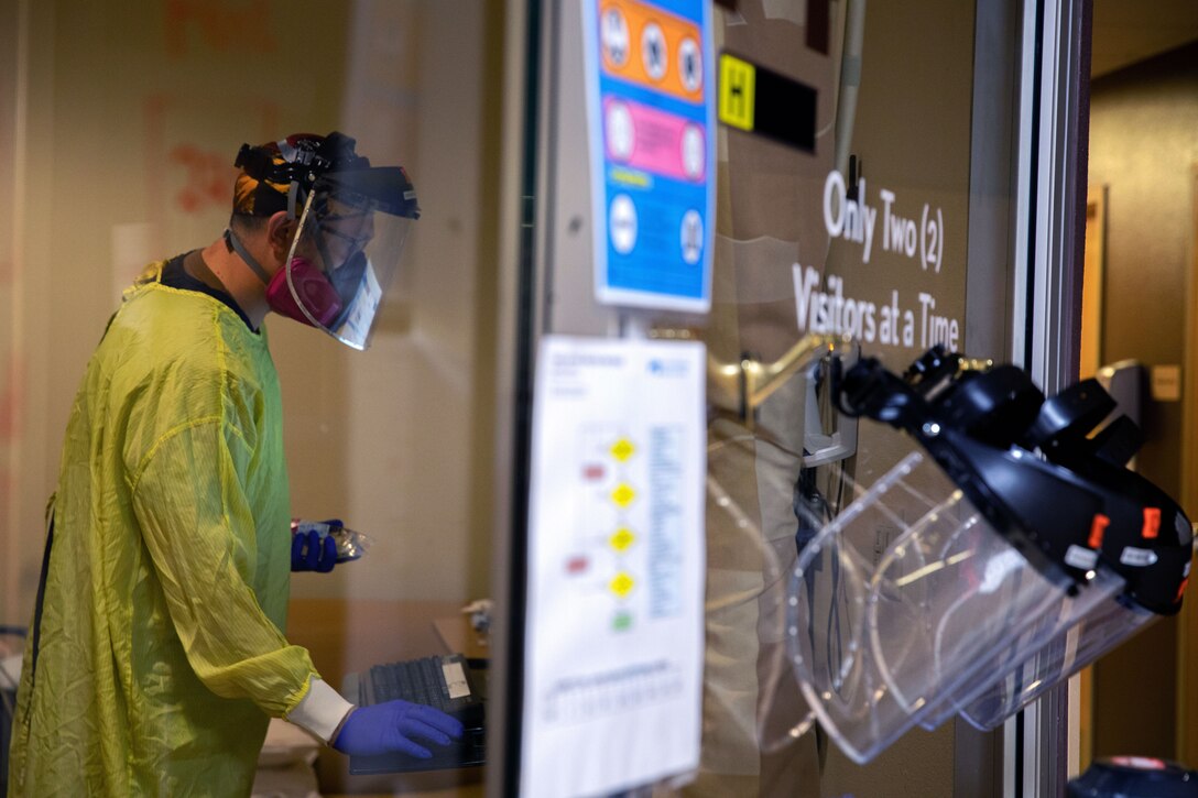 A sailor wearing personal protective equipment works on a computer.